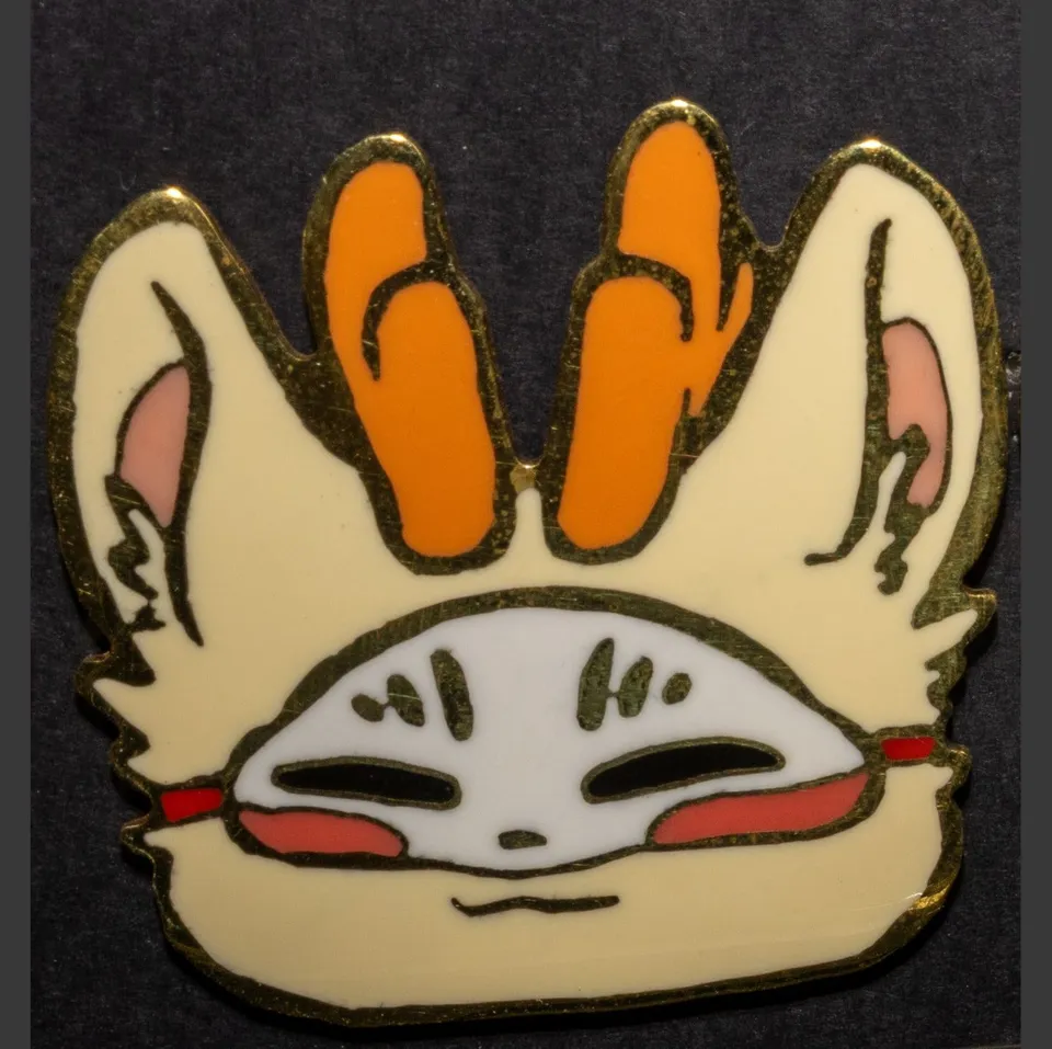 Enamel pin of a cream fox face with orange antlers and a white mask.