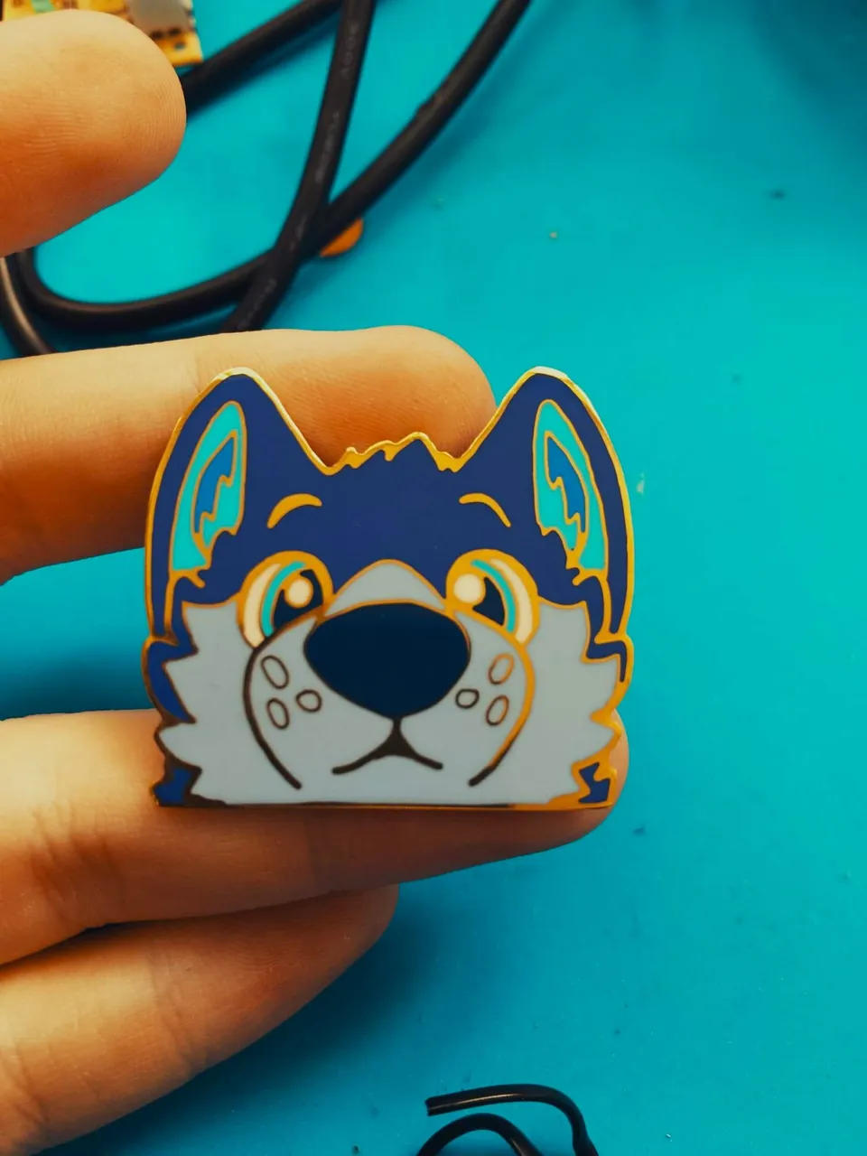 Enamel pin of a navy and pale blue wolf peeking over an edge, held between two fingers.