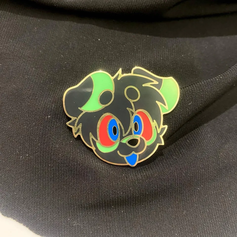 Enamel pin of a dark grey pup with lime green ears and cheeks, red and blue eyes and a blue tongue, gold outlines.
